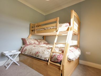 A bunk bed with patterned bedding and a small white side table in a bedroom at Rose Cottage Elsdon