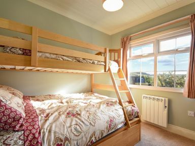 A bedroom with a wooden bunk bed and a window with curtains at Rose Cottage Elsdon