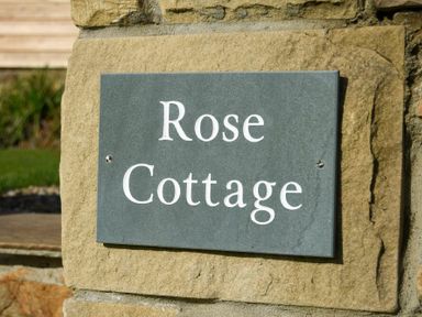 A stone wall with a slate sign reading Rose Cottage at Rose Cottage Elsdon