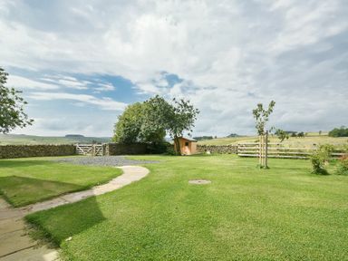A garden with a stone wall wooden shed trees and a grass path at Rose Cottage Elsdon
