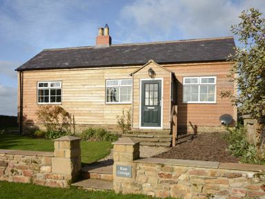 A wooden cottage with a front door steps and a stone wall in the garden at Rose Cottage Elsdon