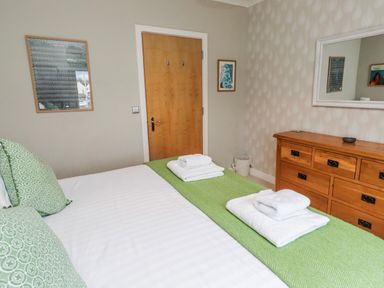 A bedroom with a bed, pillows, towels, and wooden furniture at Cuddy's Holm in Seahouses