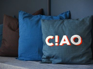 A set of four pillows on a sofa with one pillow displaying the word CIAO