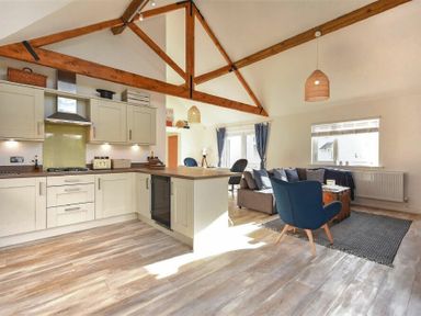 An open plan kitchen and living area with wood beams and furniture at Bowline Cottage in Beadnell