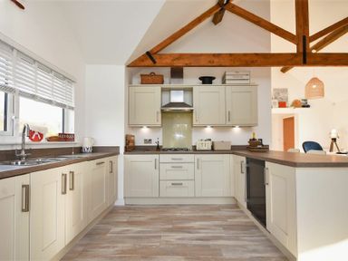 A kitchen with beige cabinets wooden beams and a window with blinds at Bowline Cottage in Beadnell