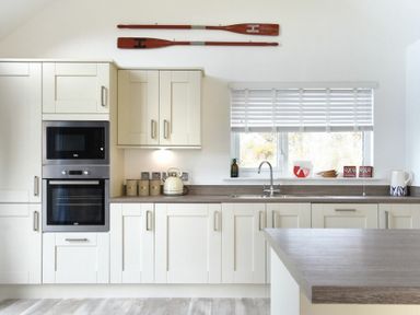 A kitchen with white cabinets a countertop microwave oven and window blinds at Bowline Cottage in Beadnell