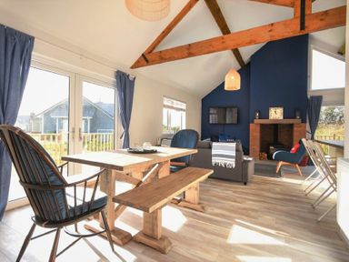 A living room with wooden dining table bench and chairs a sofa a fireplace and a television at Bowline Cottage in Beadnell