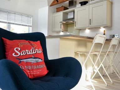 A kitchen with a blue armchair and a red cushion with sardine text at Bowline Cottage in Beadnell