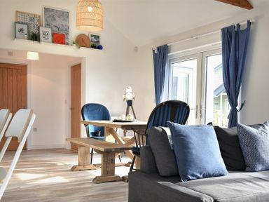 A living room with a wooden dining table blue chairs blue curtains and a gray sofa with blue cushions at Bowline Cottage in Beadnell