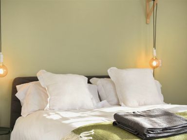 A bed with white pillows and folded grey towels on a green blanket with hanging light bulbs at Bowline Cottage in Beadnell