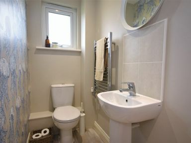 A small bathroom with a toilet sink towel rack and decorative wallpaper at Bowline Cottage in Beadnell