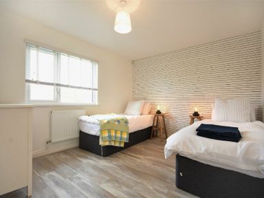 A bedroom with two single beds bedside tables and a window at Bowline Cottage in Beadnell