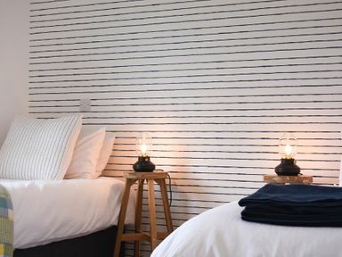 A bedroom with two beds lamps on wooden stools and a striped wall at Bowline Cottage in Beadnell