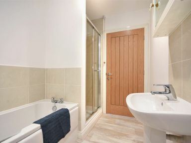 A bathroom with a bathtub a towel a shower a sink and a wooden door at Bowline Cottage in Beadnell