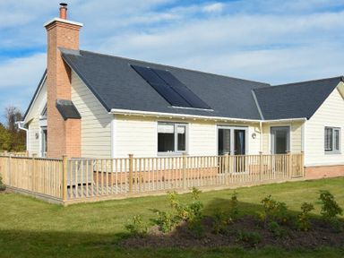 An exterior view of a single-story house with solar panels on the roof and a wooden railing around the patio at Bowline Cottage in Beadnell