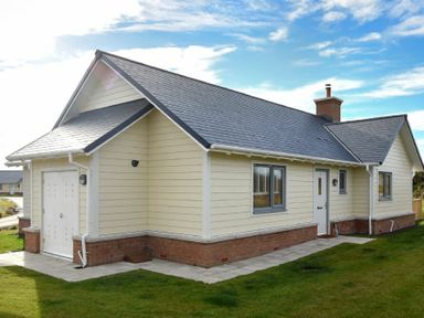 An exterior view of a single-story house with cream siding brick foundation and a dark gray roof at Bowline Cottage in Beadnell
