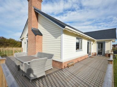 A wooden deck with outdoor table and chairs attached to a house with a brick chimney at Bowline Cottage in Beadnell