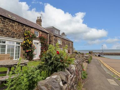 An outdoor area with stone walls and flowers at Coble Cottage in Craster