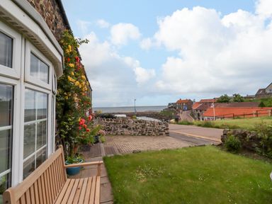 A view of a garden with a bench and flowers at Coble Cottage in Craster