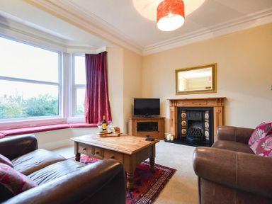 A living room with two brown sofas a wooden coffee table a fireplace and large bay windows at Sunnybrae in Alnmouth