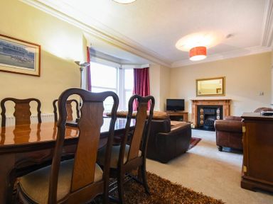 A dining area with wooden chairs and table next to a living room with leather sofas a fireplace and a television at Sunnybrae Alnmouth