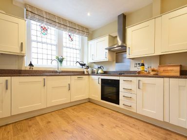 A kitchen with white cabinets an oven flowers on the counter and stained glass windows at Sunnybrae Alnmouth
