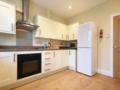 A kitchen with white cabinets a black oven a white refrigerator and a wooden floor at Sunnybrae in Alnmouth