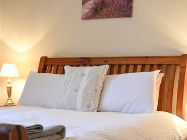 A bed with white pillows and a wooden headboard next to a lamp at Sunnybrae Alnmouth
