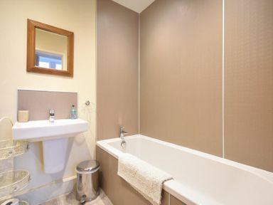 A bathroom with a bathtub a sink mirror and a trash bin at Sunnybrae Alnmouth