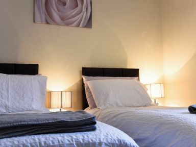 A bedroom with two single beds side by side with white bedding and lamps on each side at Sunnybrae Alnmouth