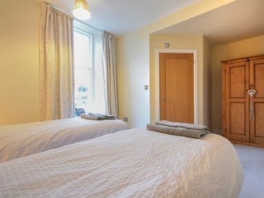 A bedroom with two single beds and towels on them near a window and wooden wardrobe at Sunnybrae Alnmouth