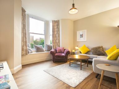 A living room with a gray sofa with yellow cushions a purple armchair a coffee table and a window seat with cushions at Sandybrae in Alnmouth