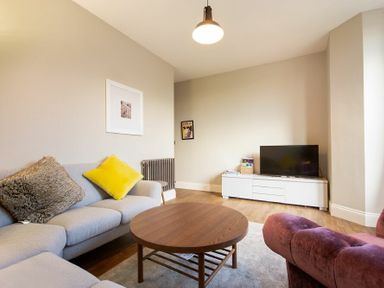 A living room with a gray sofa with cushions a round wooden coffee table a white TV stand and a flat screen TV at Sandybrae in Alnmouth