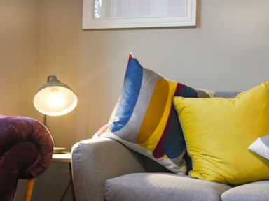 A corner of a living room with a gray sofa featuring colorful cushions and a lit table lamp on a side table at Sandybrae in Alnmouth