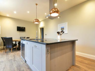 A kitchen with an island counter having a sink and utensils beside a dining table with chairs at Sandybrae in Alnmouth