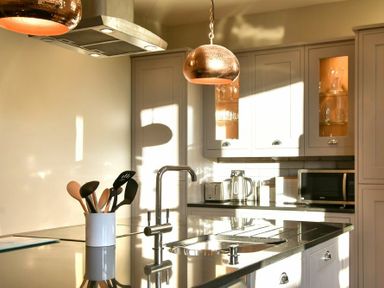 A kitchen with utensils in a container on a counter and cupboards with glass doors at Sandybrae in Alnmouth