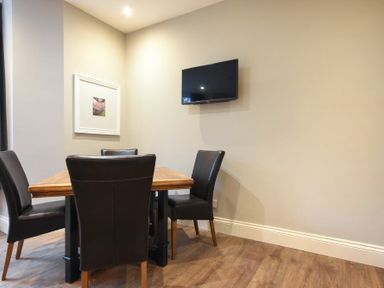 A dining area with a wooden table four black chairs a wall-mounted TV and a framed picture at Sandybrae in Alnmouth