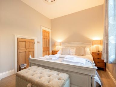 A bedroom with a double bed two bedside tables with lamps folded towels and a cushioned bench at Sandybrae in Alnmouth
