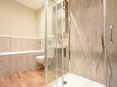 A bathroom with a bathtub wall mounted toilet shower enclosure and wooden floor at Sandybrae in Alnmouth