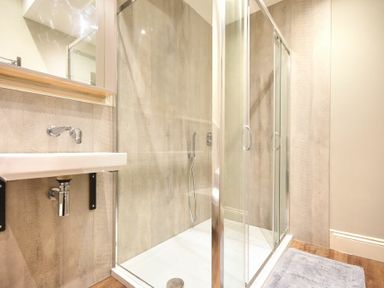 A bathroom with a glass shower enclosure a wall-mounted sink and a gray bath mat on the floor at Sandybrae in Alnmouth