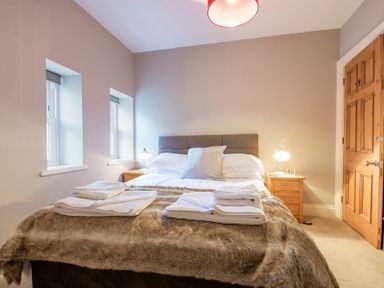 A bedroom with a bed between two windows and wooden door at Sandybrae in Alnmouth