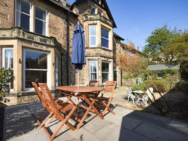 An outdoor patio area with wooden table and chairs and a blue umbrella in front of a stone house at Sandybrae in Alnmouth
