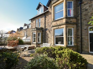 A stone house exterior with windows a white bench metal chairs and table and a wooden deck with furniture at Sandybrae in Alnmouth