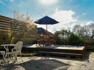 An outdoor patio area with wooden chairs and table under a blue umbrella and a white metal table with chairs at Sandybrae in Alnmouth