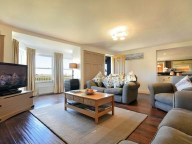 A living room with three armchairs a wooden coffee table a television and large windows at Mariners House in Alnmouth
