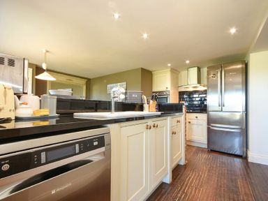 A kitchen with cream cabinets black countertops stainless steel appliances and wooden flooring at Mariners House in Alnmouth