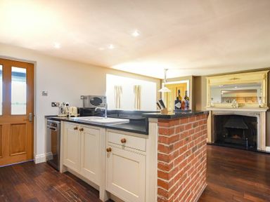 A kitchen with a sink and countertop appliances with a brick bar and a fireplace in the background at Mariners House in Alnmouth