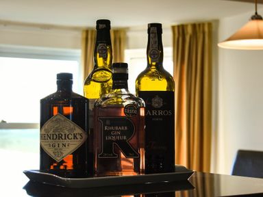 Bottles of gin and liqueur on a tray on a table in a dining area with yellow curtains and a hanging lamp at Mariners House in Alnmouth