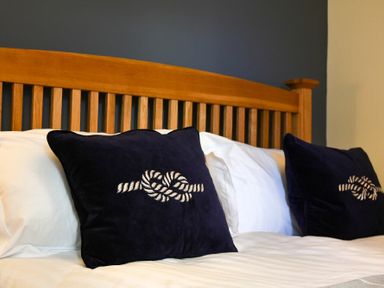 A wooden headboard with two dark pillows featuring knot designs on a bed with white linens at Mariners House in Alnmouth