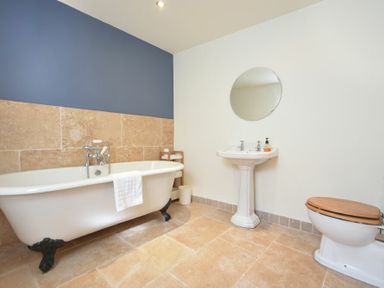 A bathroom with a freestanding bathtub, pedestal sink with round mirror, and toilet with wooden seat at Mariners House in Alnmouth